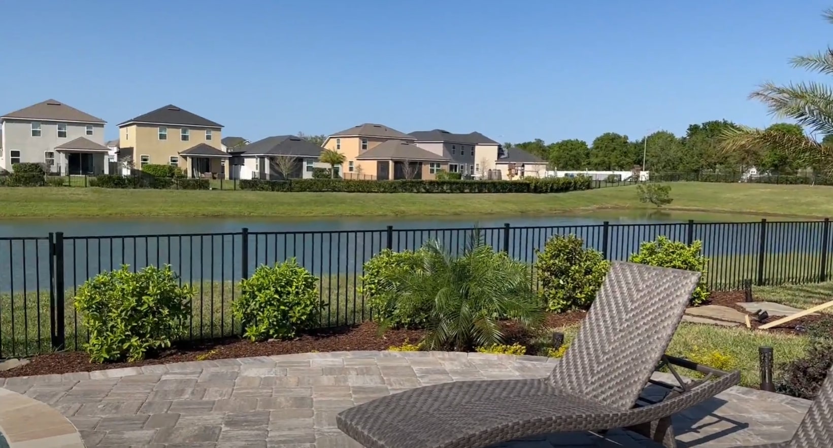 Waterfront landscape design combining privacy fencing with decorative plantings and entertainment areas Waterfront residential landscape with black metal fencing, strategic plantings, and hardscaping featuring outdoor furniture on stone patio