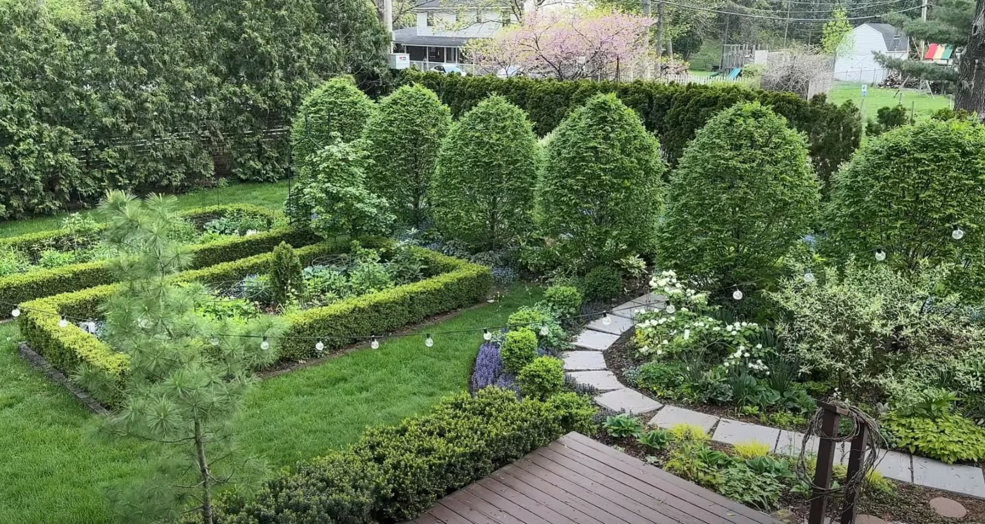 Traditional landscape design featuring formal hedge work, natural stone pathways, and mature specimen trees Formal residential garden with manicured hedge borders, stone pathways, and established shade trees creating structured outdoor rooms